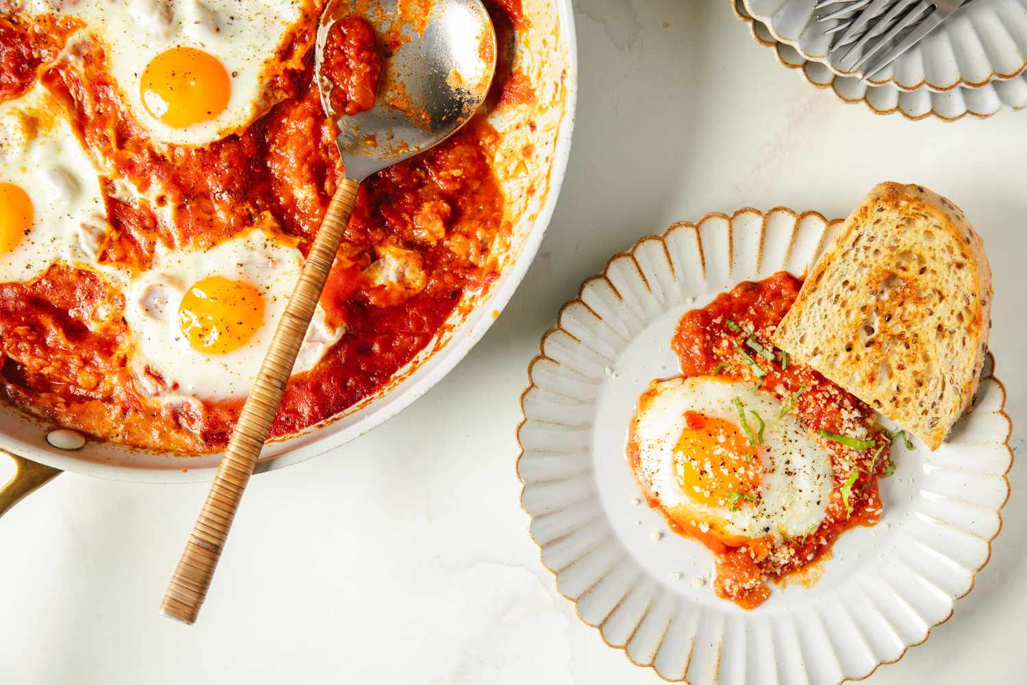 Shakshuka with sunnysideup eggs served in a skillet and a portion on a plate with bread