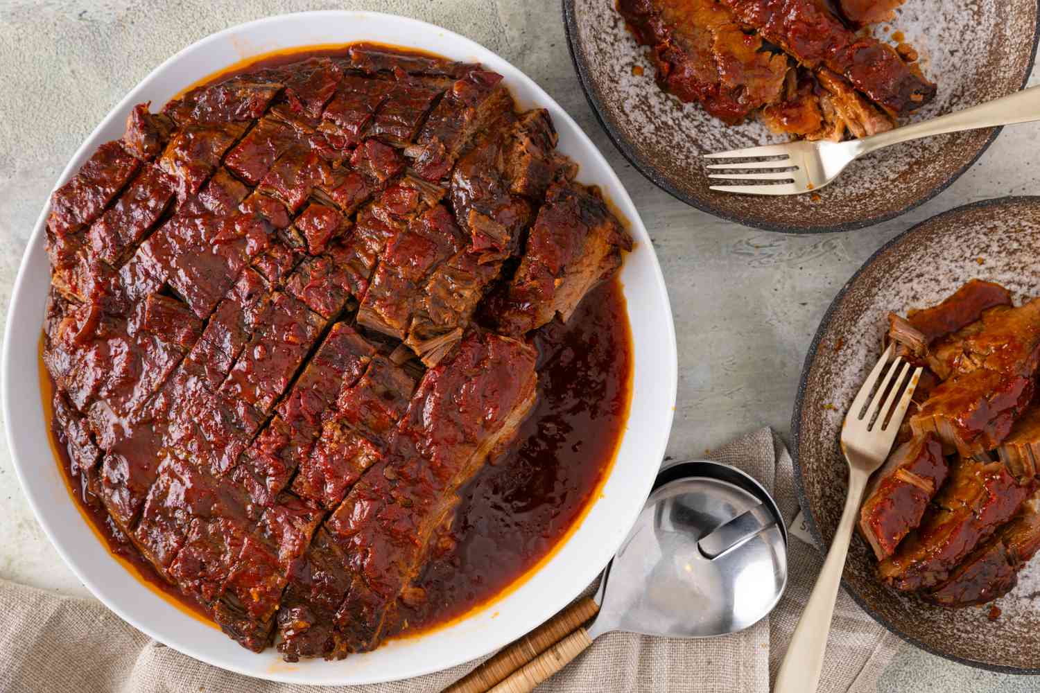 Sliced and roasted brisket on a serving plate, with two plates of brisket next to it