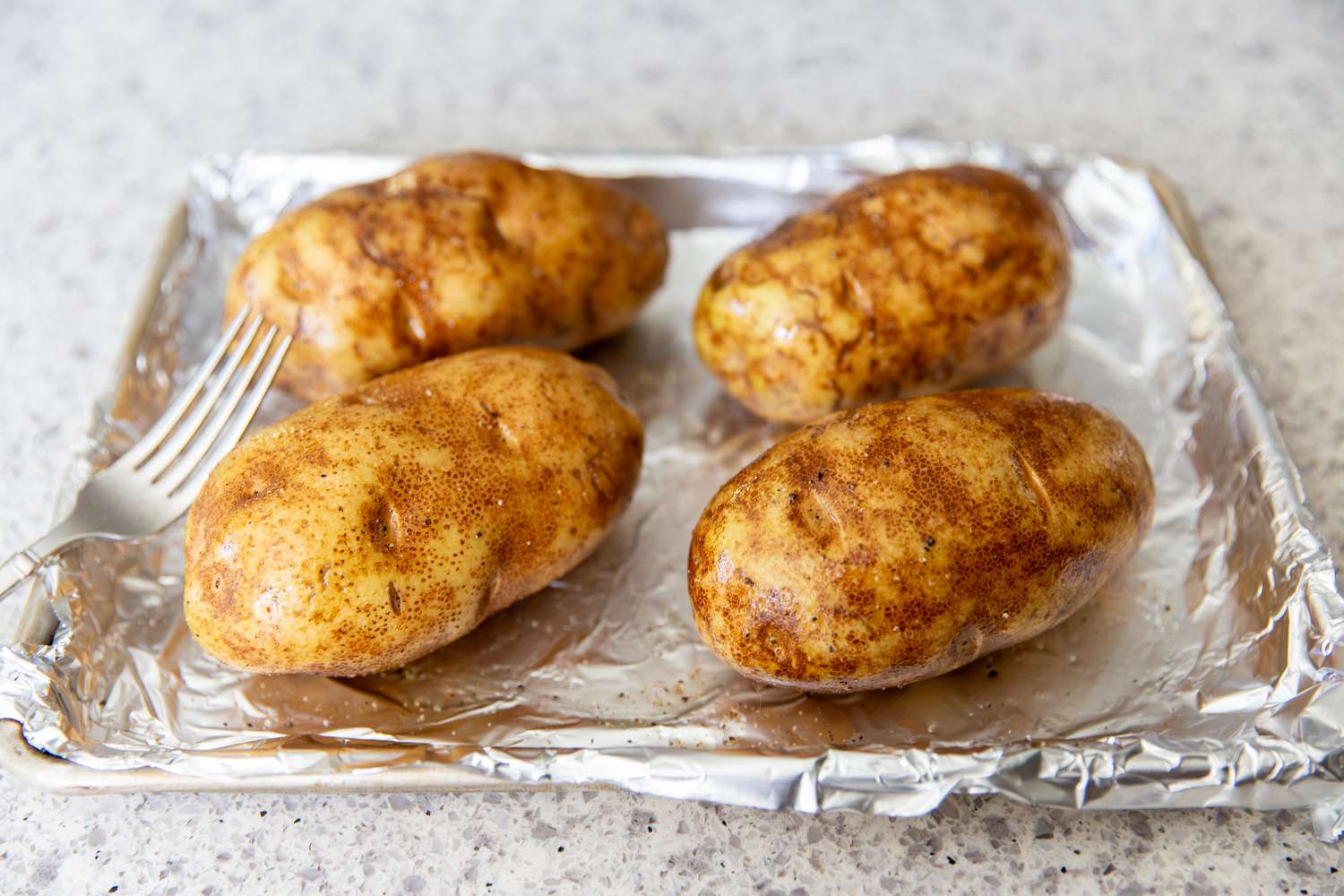 four oil rubbed potatoes on aluminum foil covered baking pan