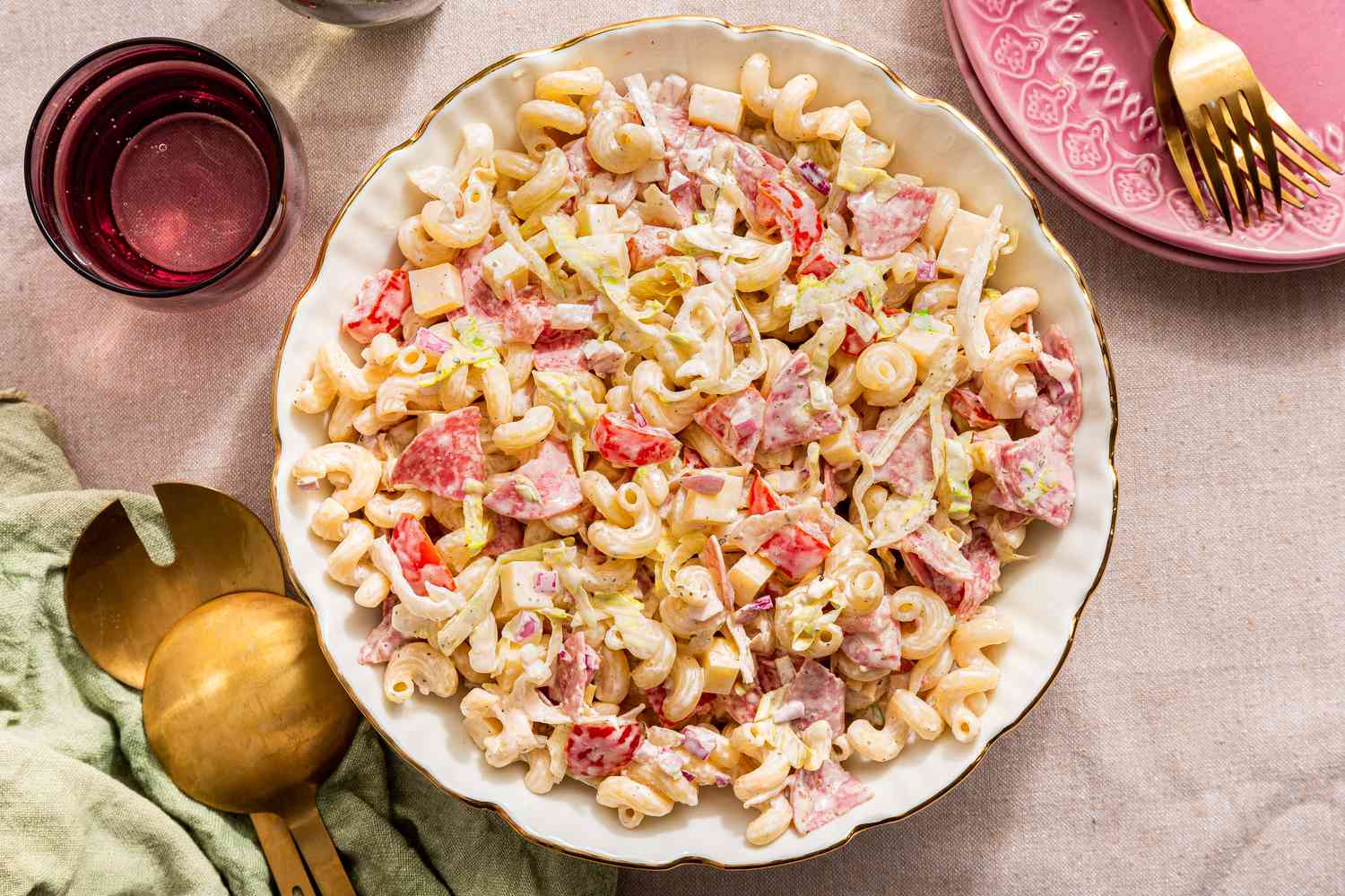 ginder pasta salad in a bowl at a table setting with glasses of water, serving utensils on a table napkin, and a stack of plates