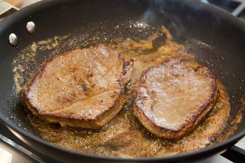 two steaks cooking in a pan