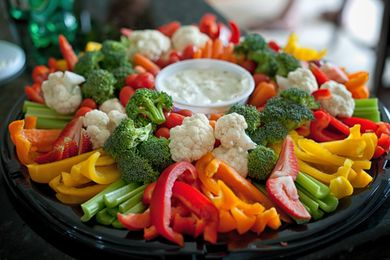 A vegetable tray with celery bell peppers broccoli cauliflower and dip in the center