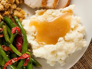 A close-up of a plate with mashed potatoes and gravy, turkey, green beans, and stuffing