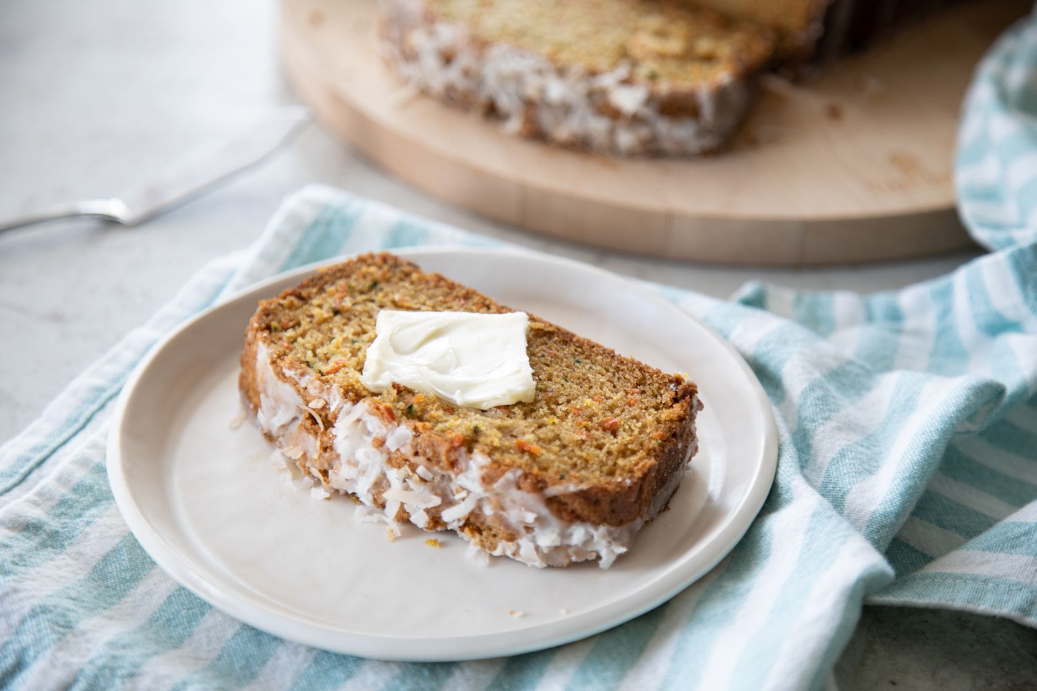 Slice of Zucchini Carrot Bread with Butter on a Plate Next to Board with More Bread