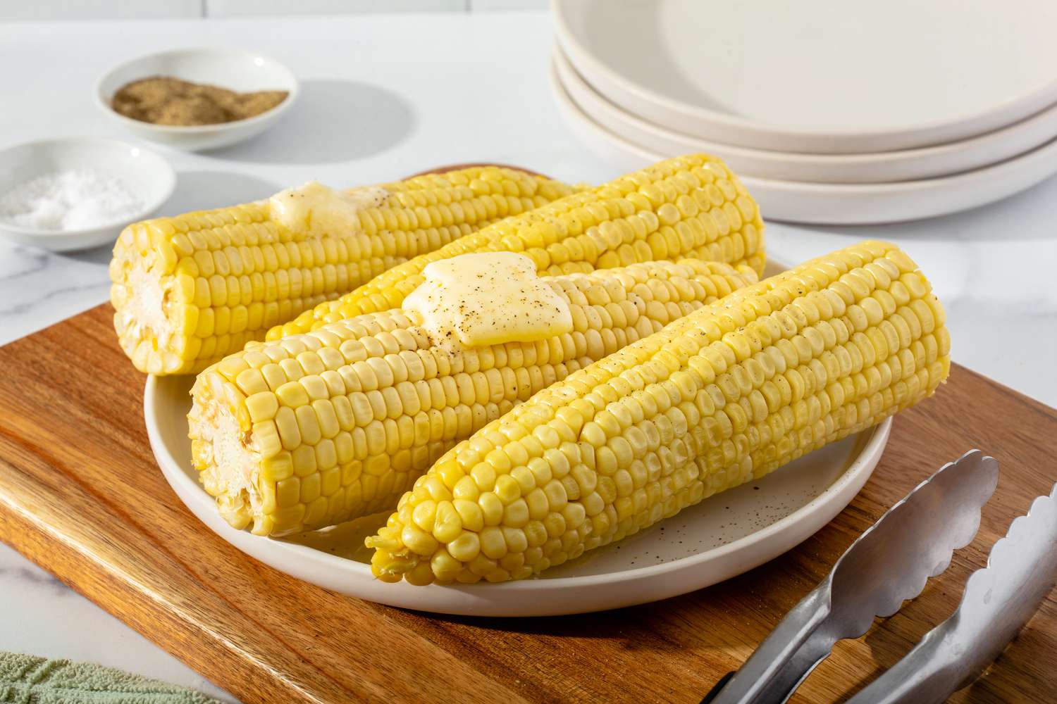 A plate of microwave corn on the cob set on a cutting board and topped with butter.