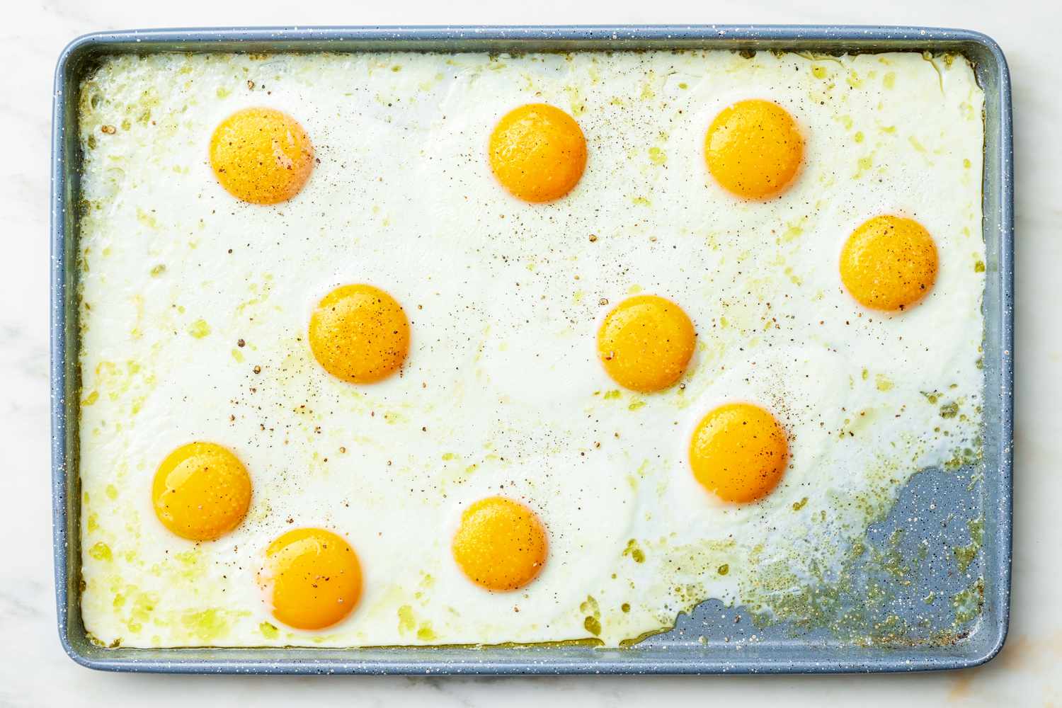 Sheet Pan Fried Eggs Topped With Cracked Pepper on a Baking Pan