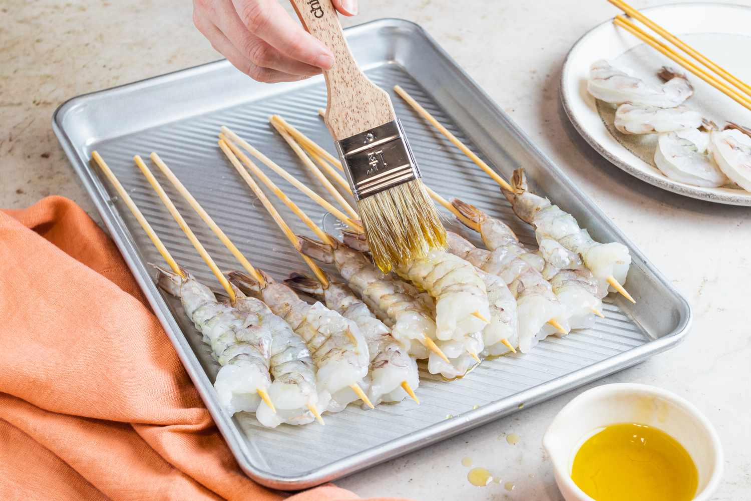 Brushing shrimp skewers with oil and setting on a baking sheet.