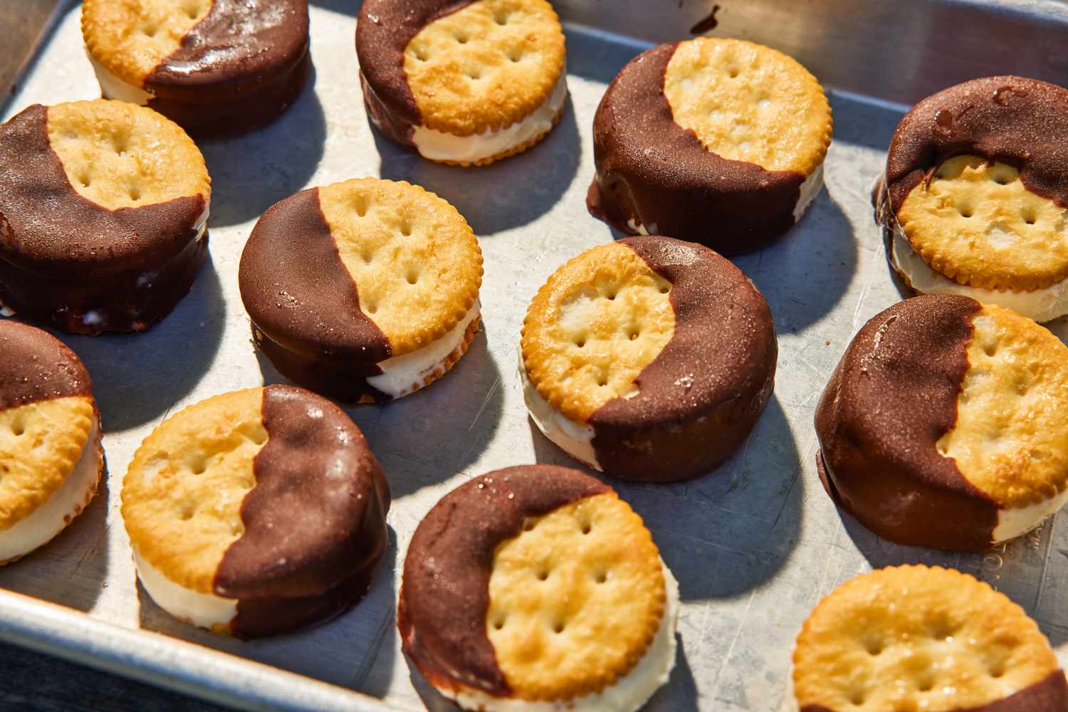 Ritz crackers assembled into ice cream sandwiches, partially dipped in chocolate, on a tray