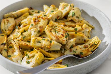 Side view closeup of a large serving plate with garlic & herb sautéed artichokes, with a spoon on the plate