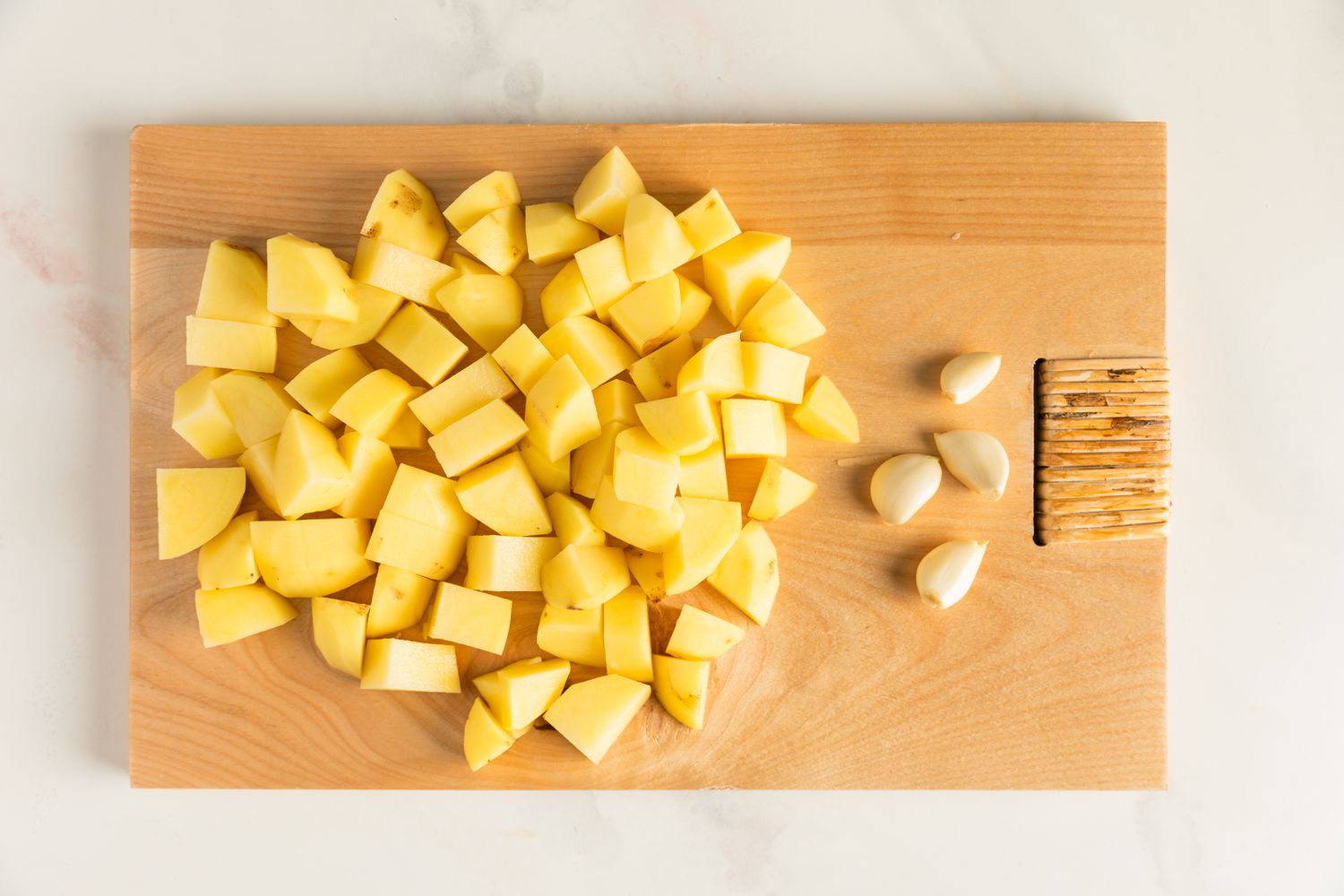 Potatoes cubed on a cutting board with peeled garlic cloves on the side