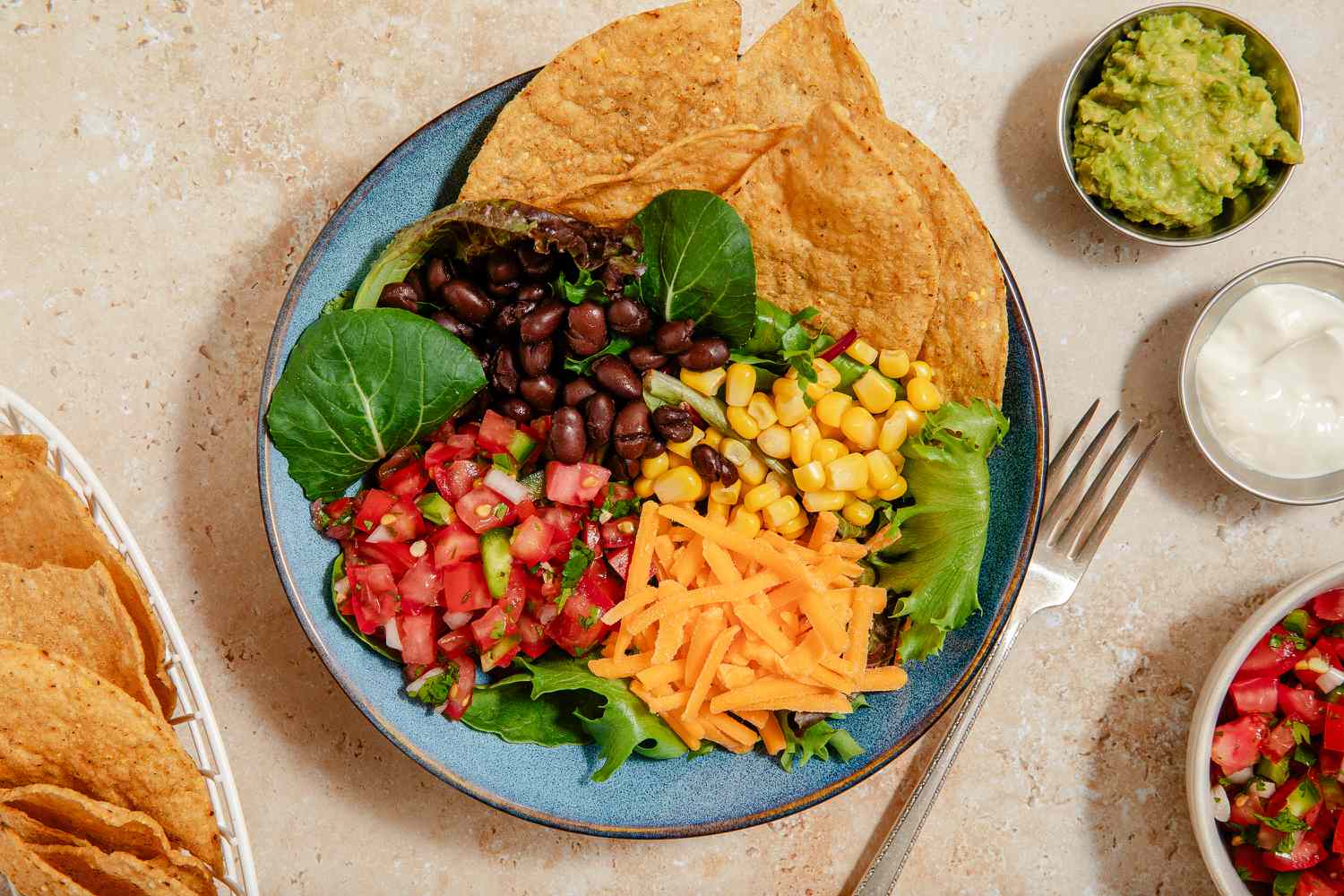 black bean nacho bowl next to a small bowls of guacamole, sour cream, and salsa and a bigger bowl with more nachos 