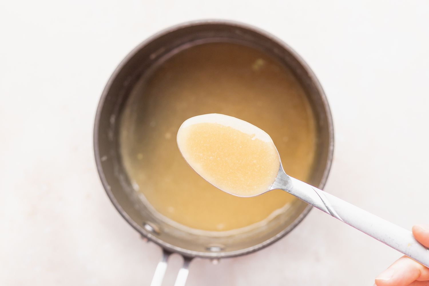 A thinner bread pudding sauce being spooned out of a saucepan.