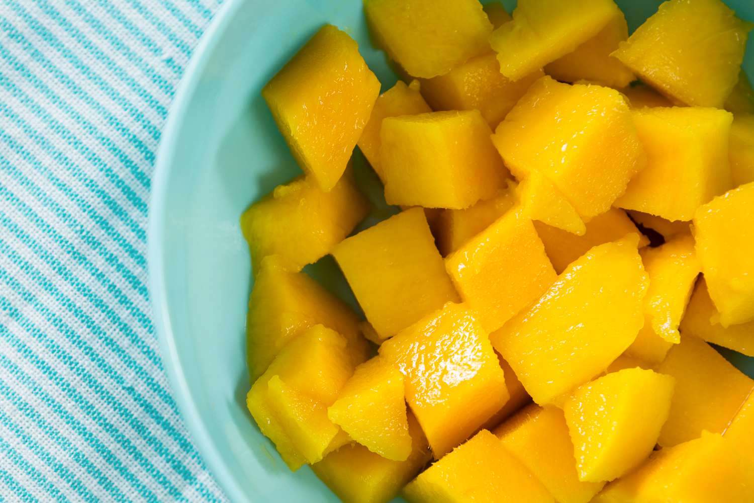 Cubed mango pieces in a blue bowl on a light blue striped cloth