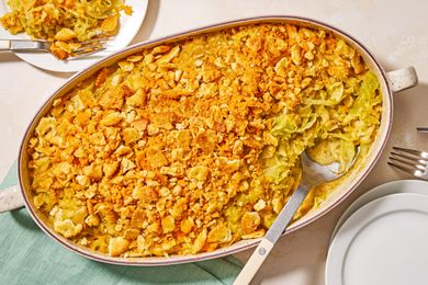 A casserole dish with cheesy cabbage casserole topped with a crunchy layer served with utensils and a green napkin nearby