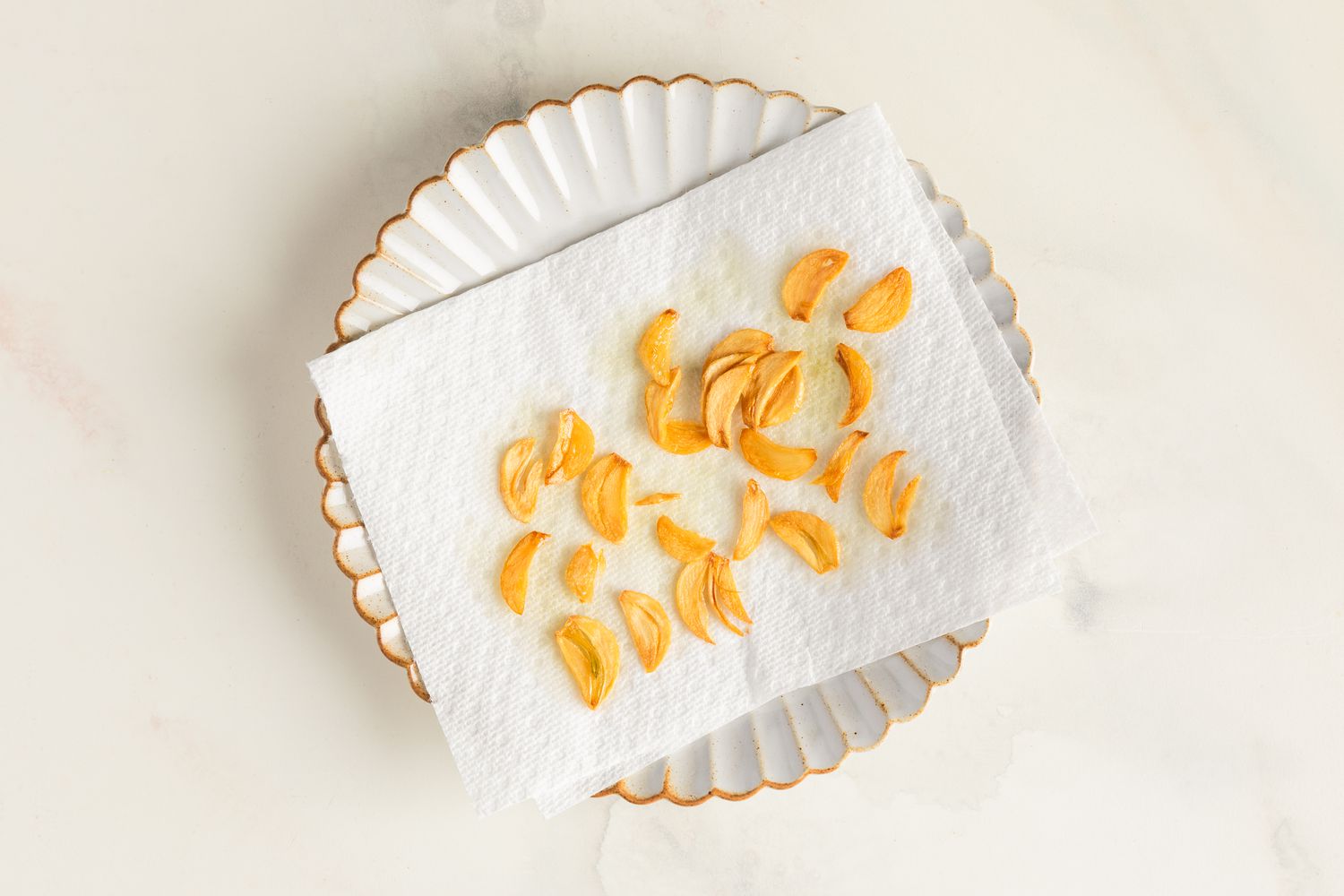 Garlic chips draining on a paper towel set on a small scalloped plate