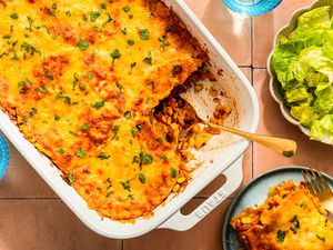 Chicken taco casserole (with a serving cut out) at a table setting with a serving on a plate, glasses, and a side salad