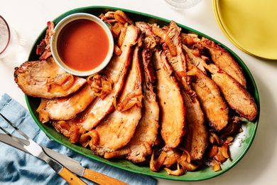 A platter of sliced brisket with onions and a dipping sauce in a small bowl