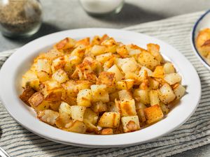 Angled view of a white bowl of breakfast potatoes in a table setting with a spoon and salt and pepper shakers in the background