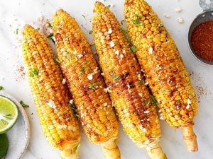 Cajun-Spiced Grilled Corn Next to a Saucer with Two Lime Halves and a Small Bowl with More Cajun Seasoning