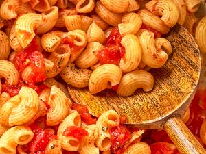 Cooked macaroni with diced tomatoes resting on a wooden spoon