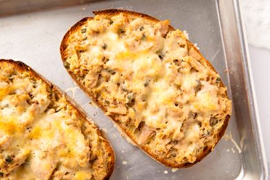 Toasted bread slices topped with a mixture of tuna and melted cheese on a baking tray