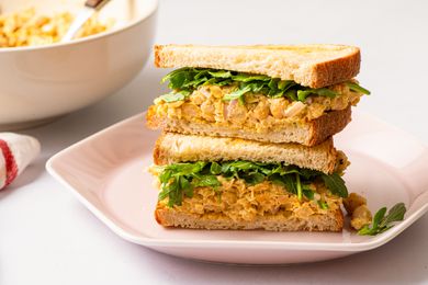 Angled view of curried chickpea salad sandwich on a pink plate, all on a white background