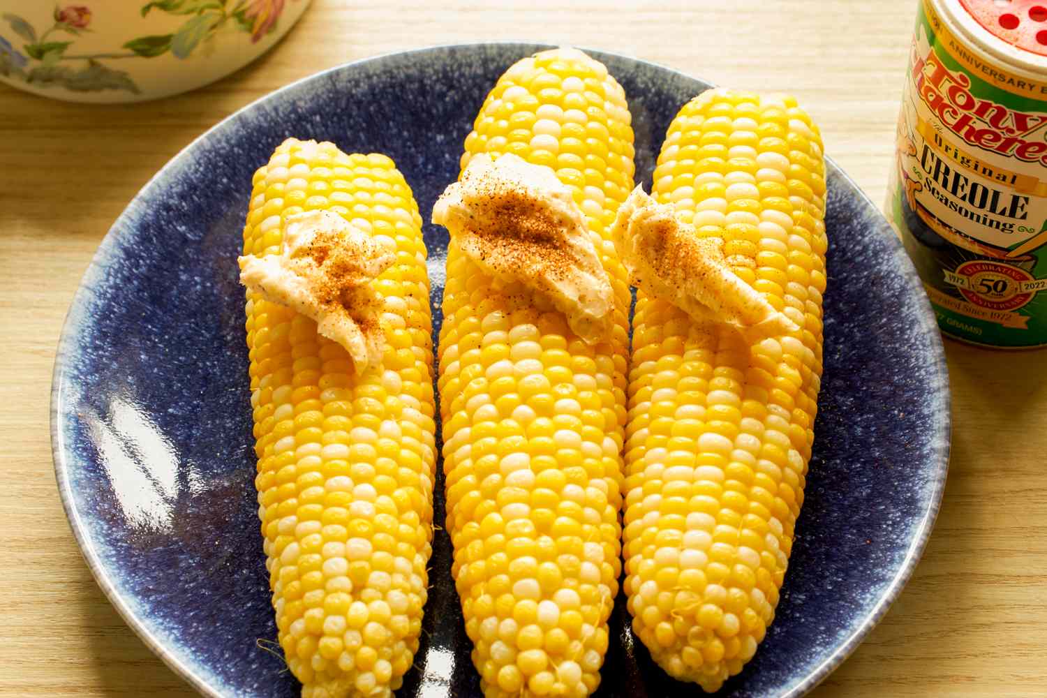 Three ears of corn with seasoning and butter on a blue plate