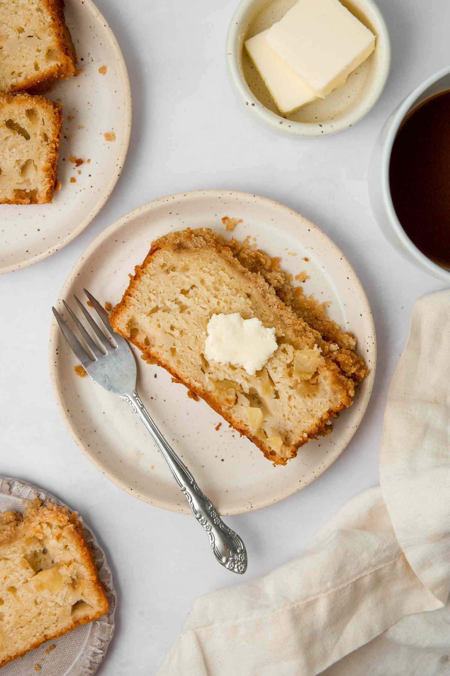Slices of cinnamon streusel apple bread on plates and topped with butter.