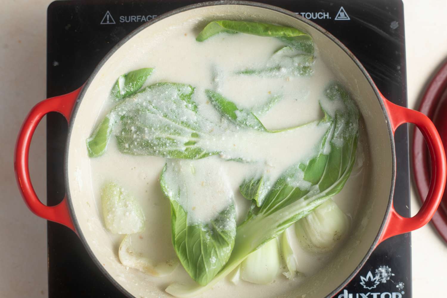 Overhead view of a dutch oven with ingredients to make coconut poached fish with bok choy, ginger, and lime