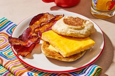 An english muffin with a slice of baked egg, and two slices on bacon on the side