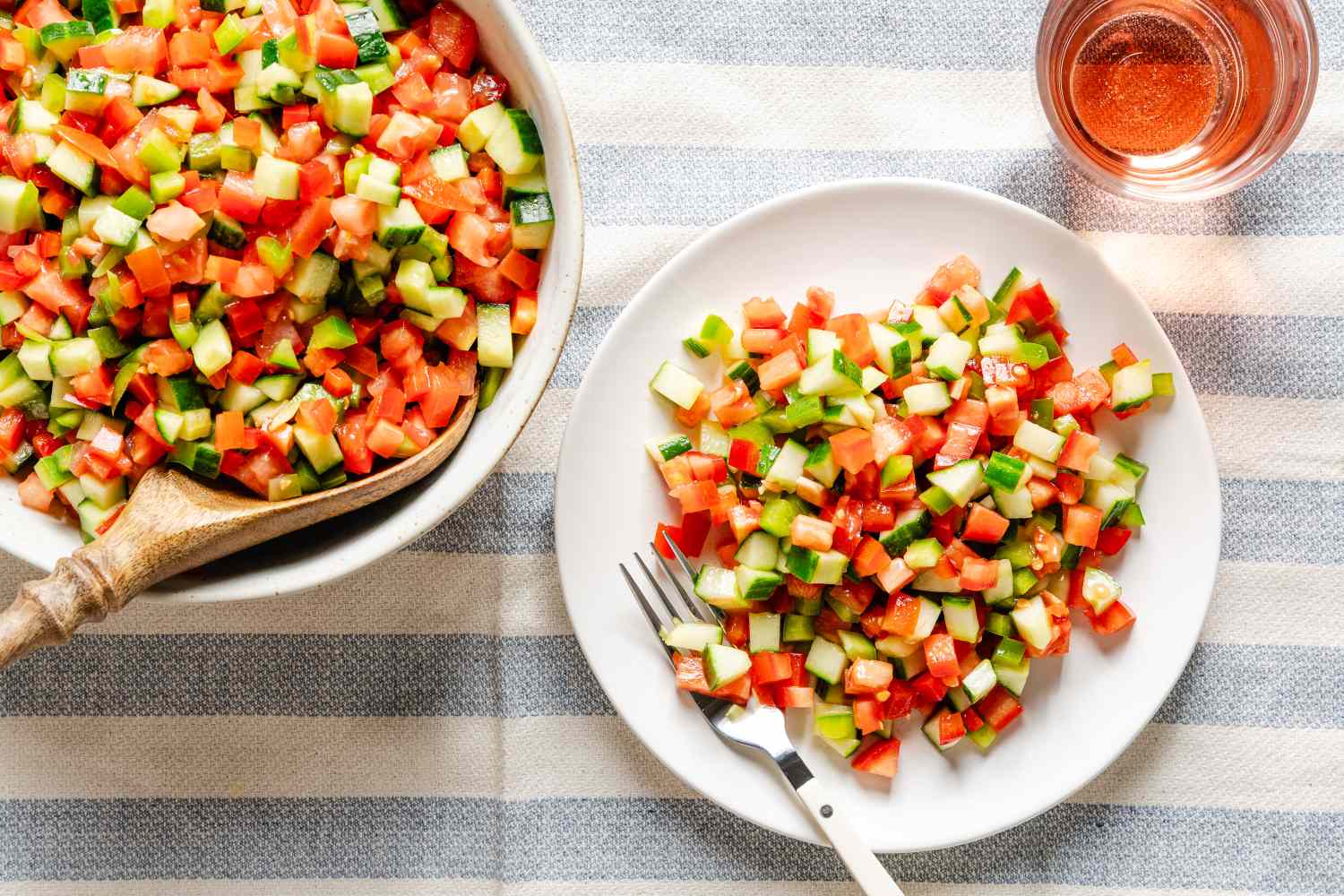 Pipirrana salad served in a bowl and on a plate with a fork placed on a striped tablecloth