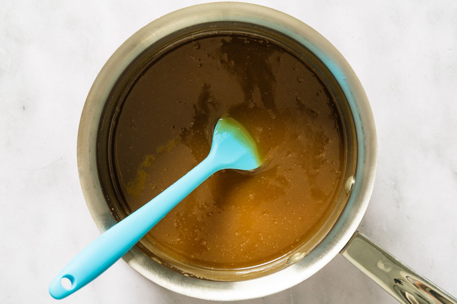 A pot containing brown sauce being stirred with a blue spatula
