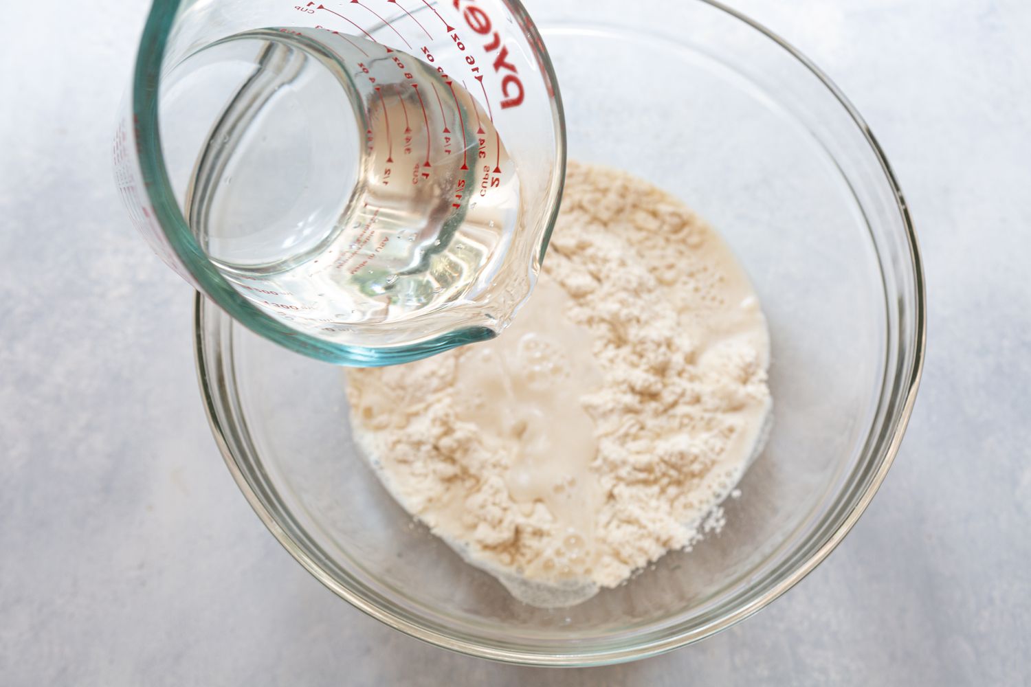 Water being pouted into flour to make dough in a glass bowl 