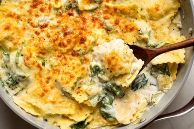 Cheesy spinach and artichoke ravioli cooked in a pan with a wooden spoon