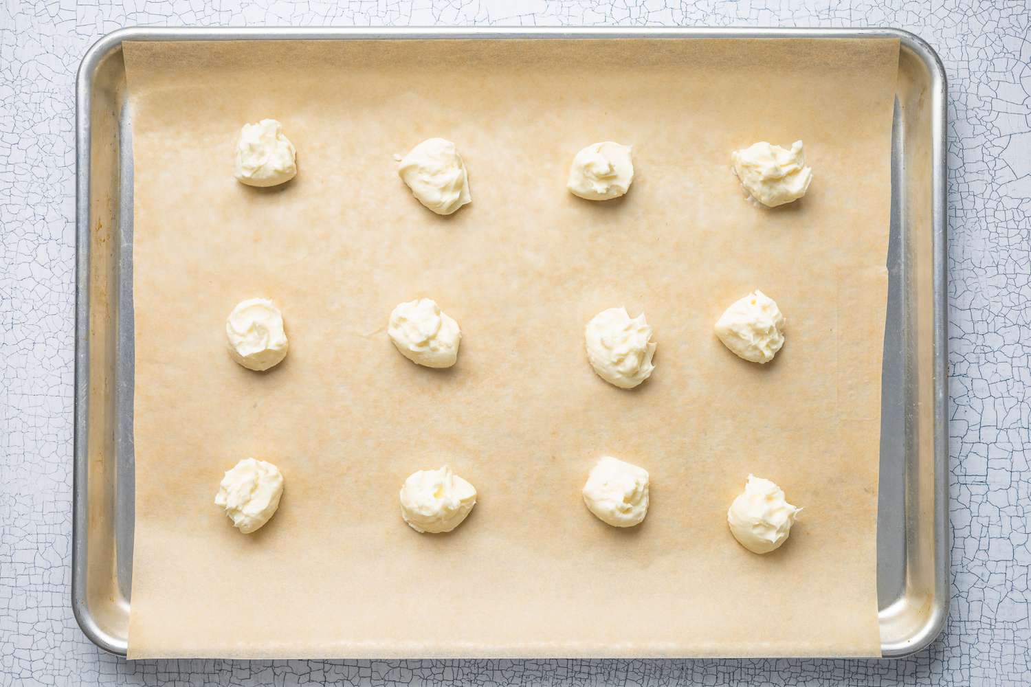 Dollops of Cream Cheese Filling on a Parchment Paper Lined Baking Pan for Strawberry Cheesecake Cookie Recipe