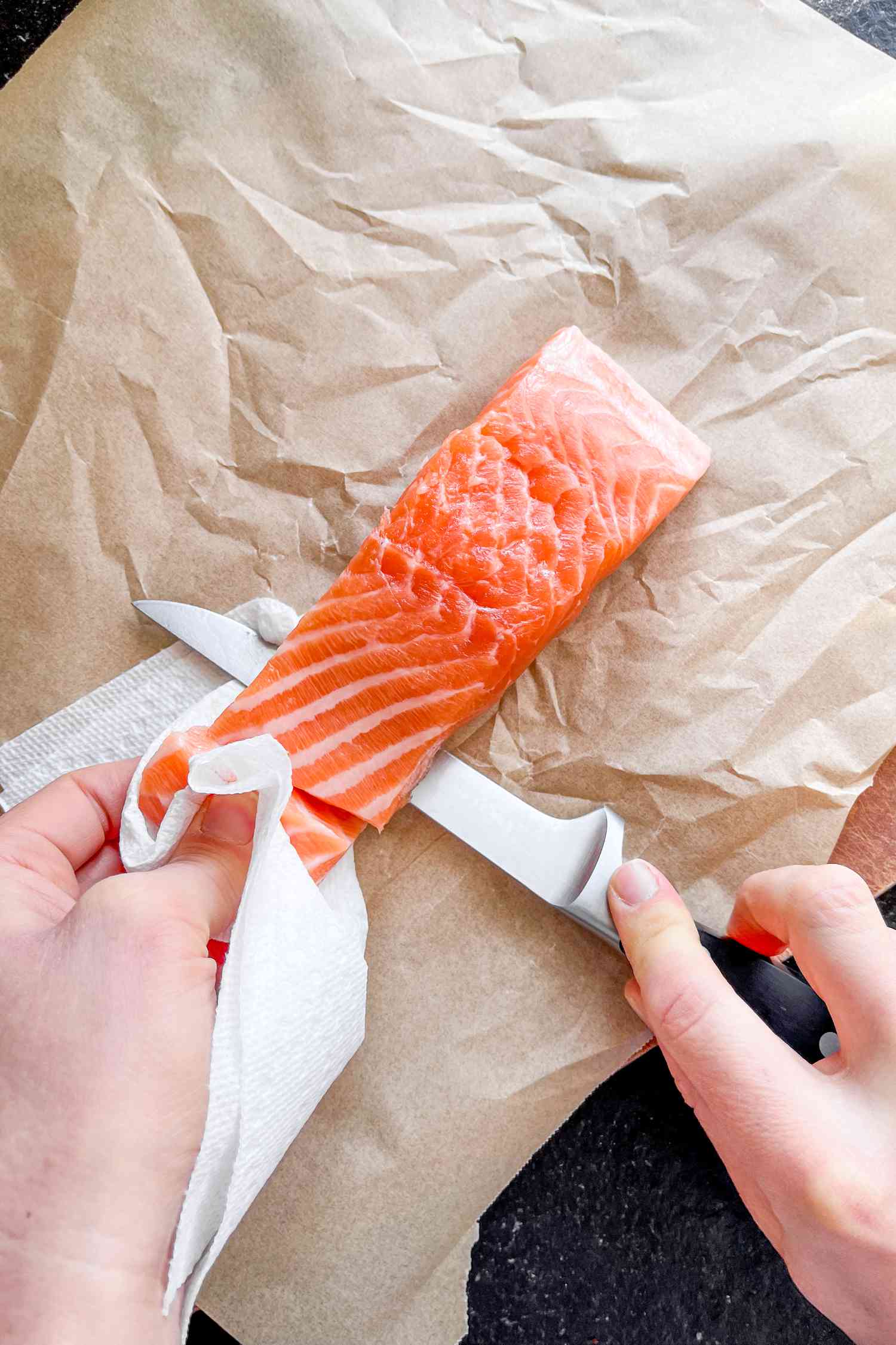 Overhead view of a salmon fillet having the skin removed with a knife