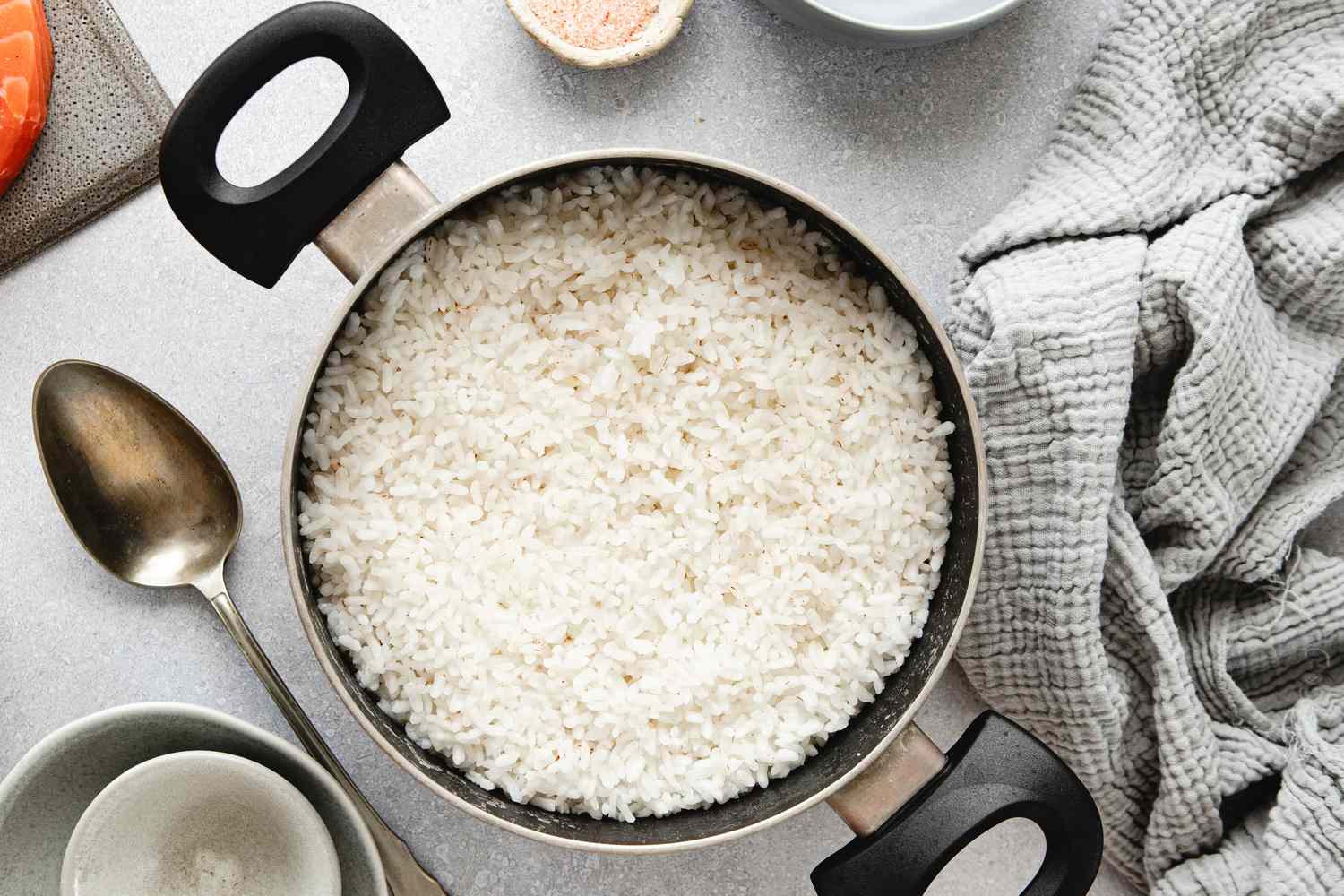 Overhead view of pot of white rice on a counter next to a serving spoon and a gray towel