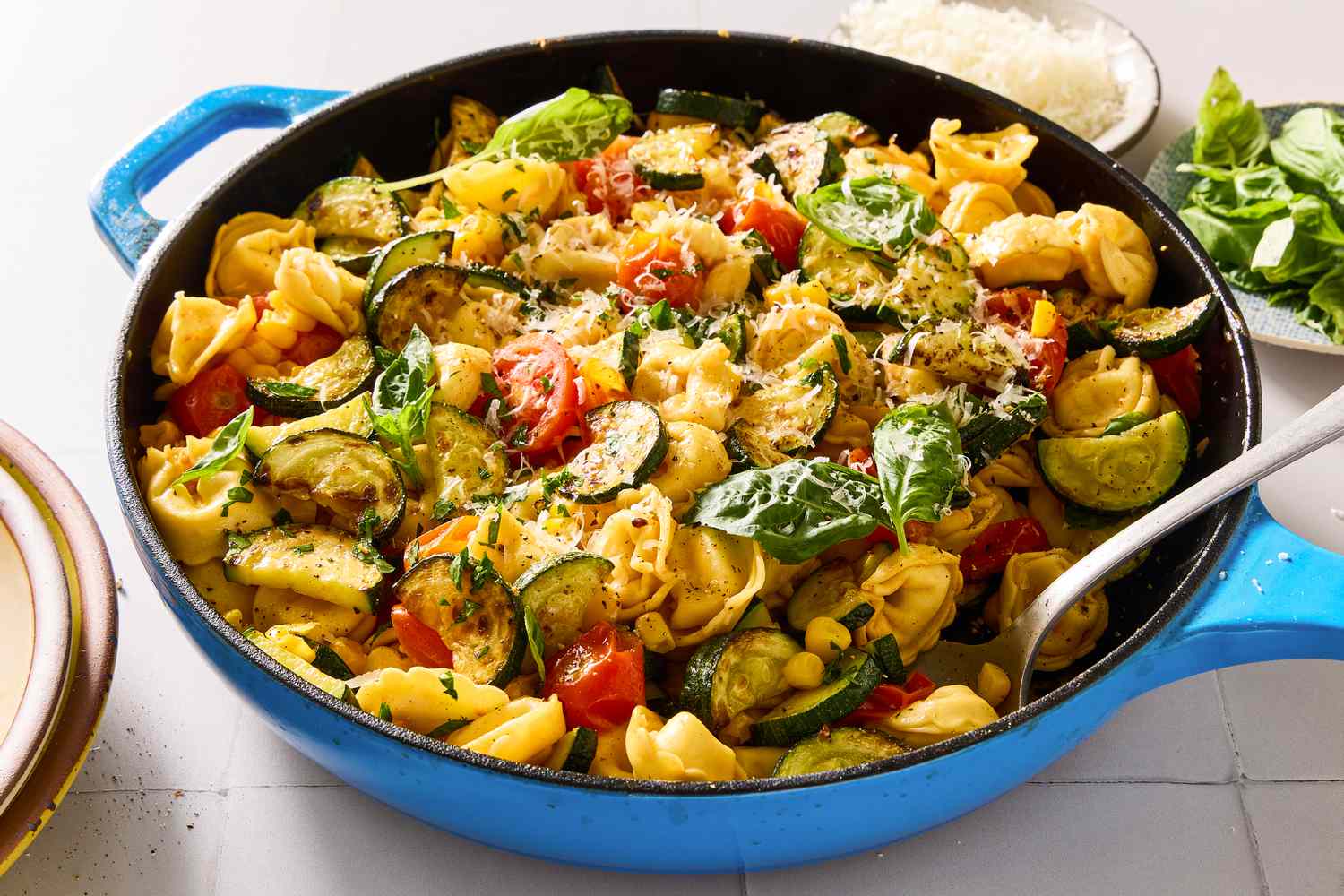 A skillet containing tortellini with vegetables and herbs, served with a spoon