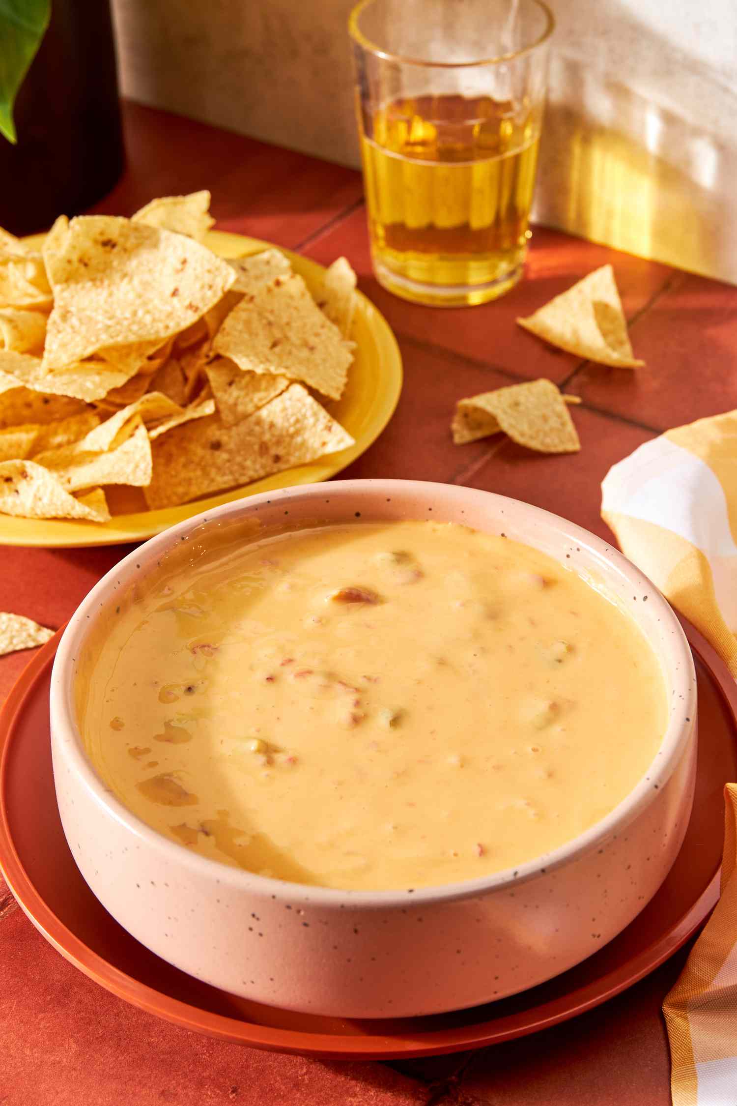 Classic 2-Ingredient Ro*Tel Queso Dip in a bowl at a table setting with a bowl of chips and a glass of beer