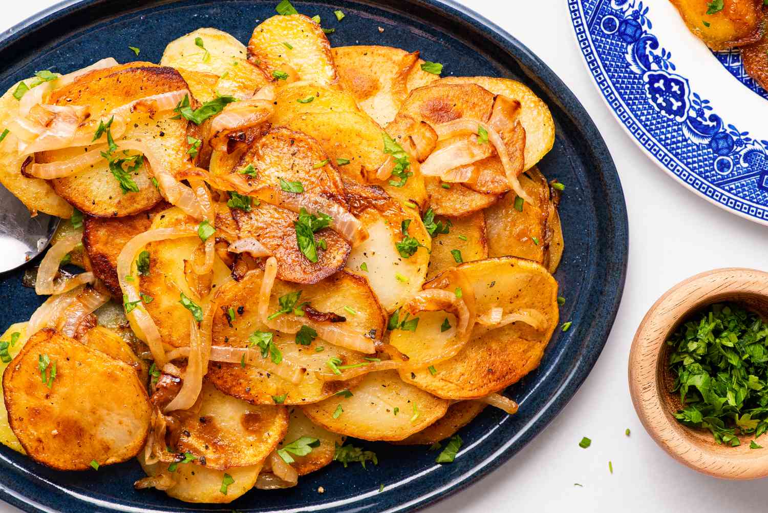 Lyonnaise potatoes on a platter at a tablet setting with a plate with a serving of potatoes and a bowl of minced parsley