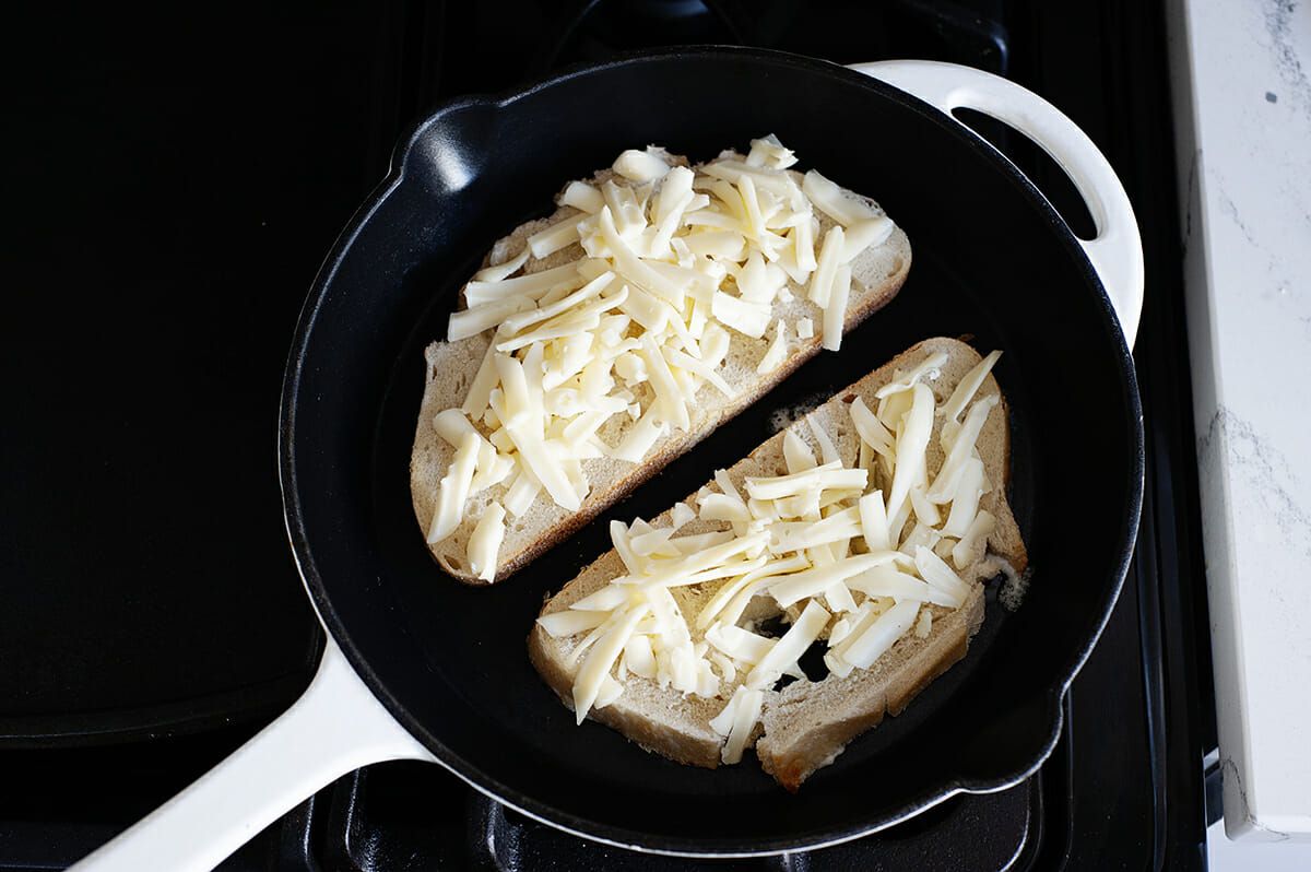 Two slices of bread, set open faced with shredded cheese on top in a cast iron skillet.