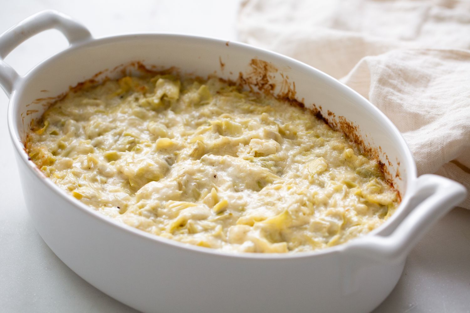 Casserole Dish With Easy Artichoke Dip Next to a Kitchen Linen