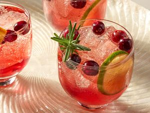 Three cranberry ginger spritz cocktails garnished with cranberries lime slices and a sprig of rosemary