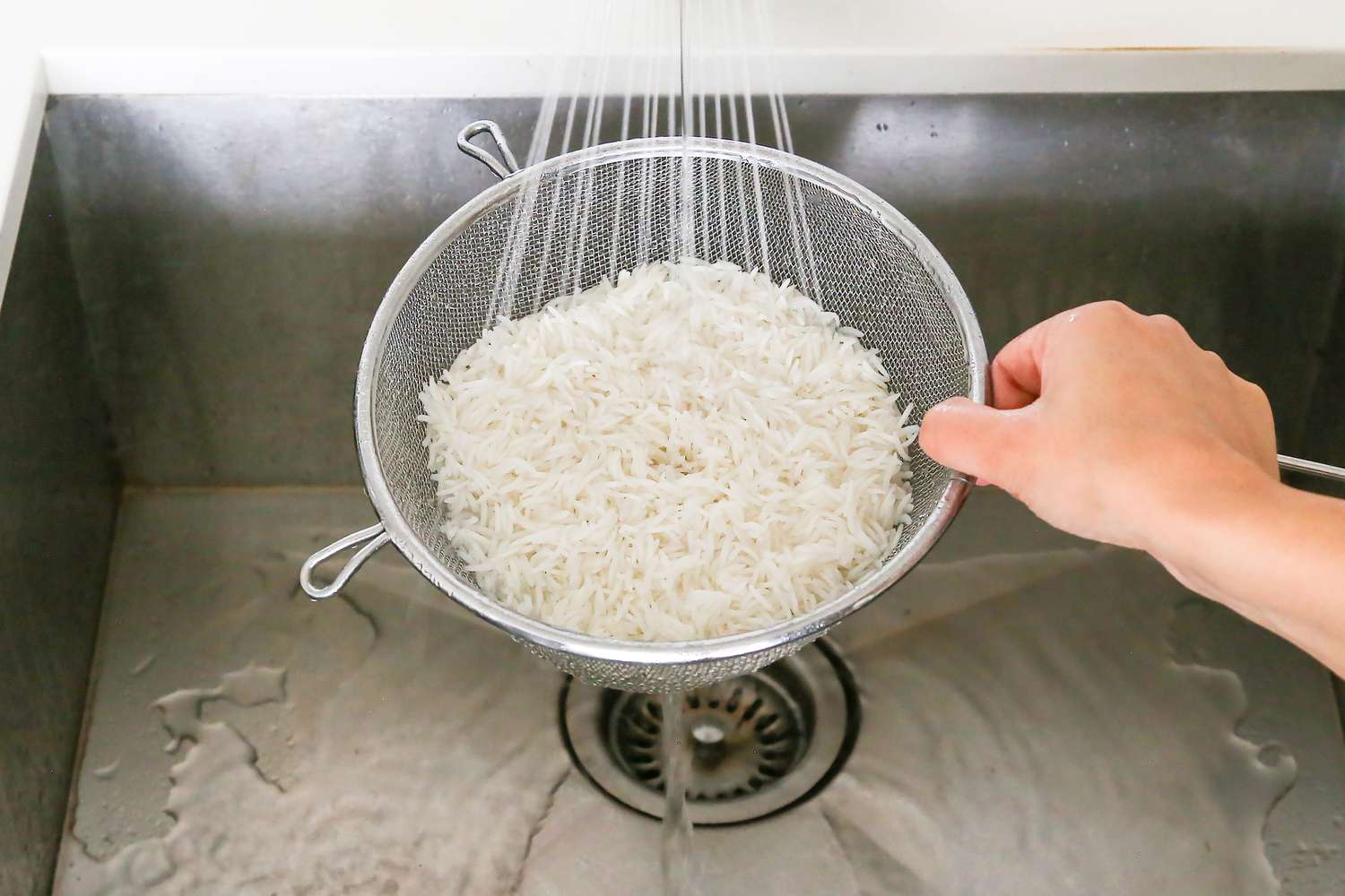 Colander of Cooked Rice Rinsed under a Running Faucet of Water 