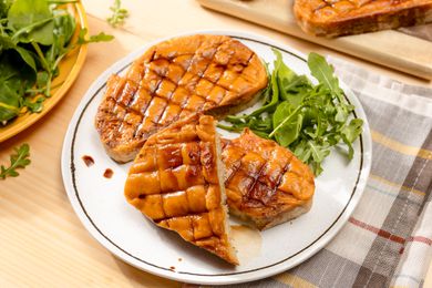 Serving of Welsh rarebit on plate with a side salad at a table with another serving on a plate and more welsh rarebit on a cutting board