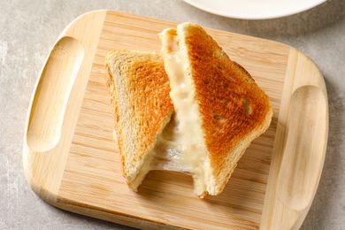 Grilled cheese sandwich on a wooden board cut into triangles with melted cheese oozing out