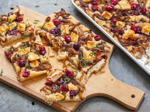 A cutting board with slices of focaccia topped with caramelized onions, cranberries, and brie.