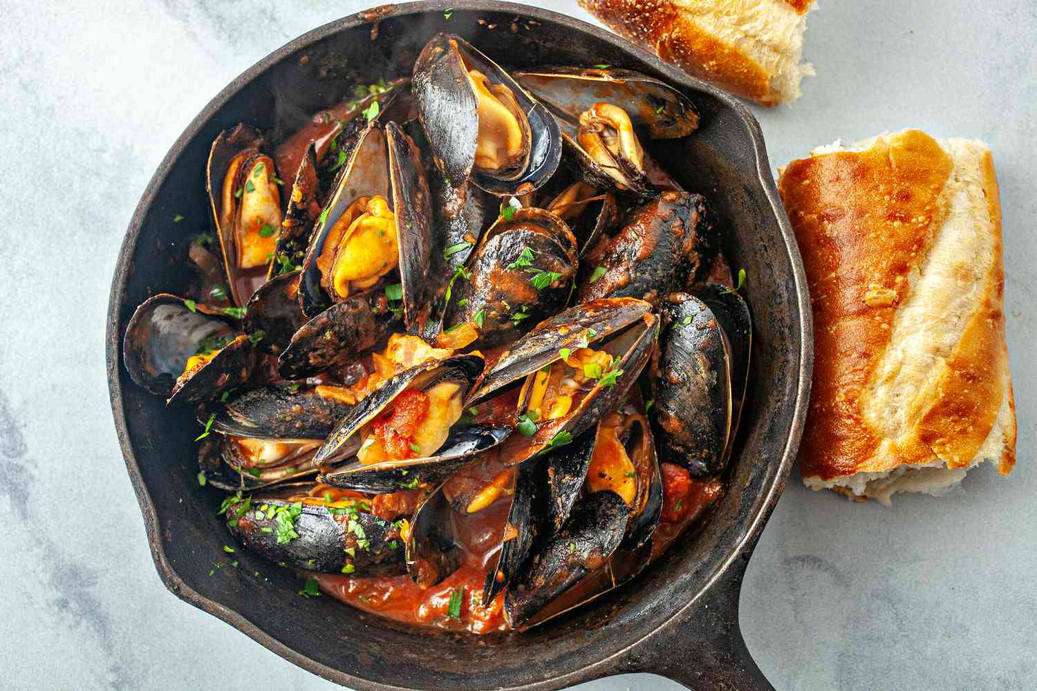 A pan of steamed mussels with tomato sauce and bread on the side