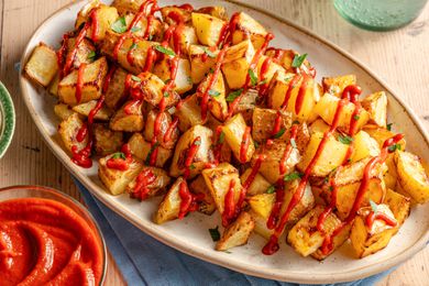Angled view of a platter of patatas bravas topped with sauce and parsley all on a wooden table top