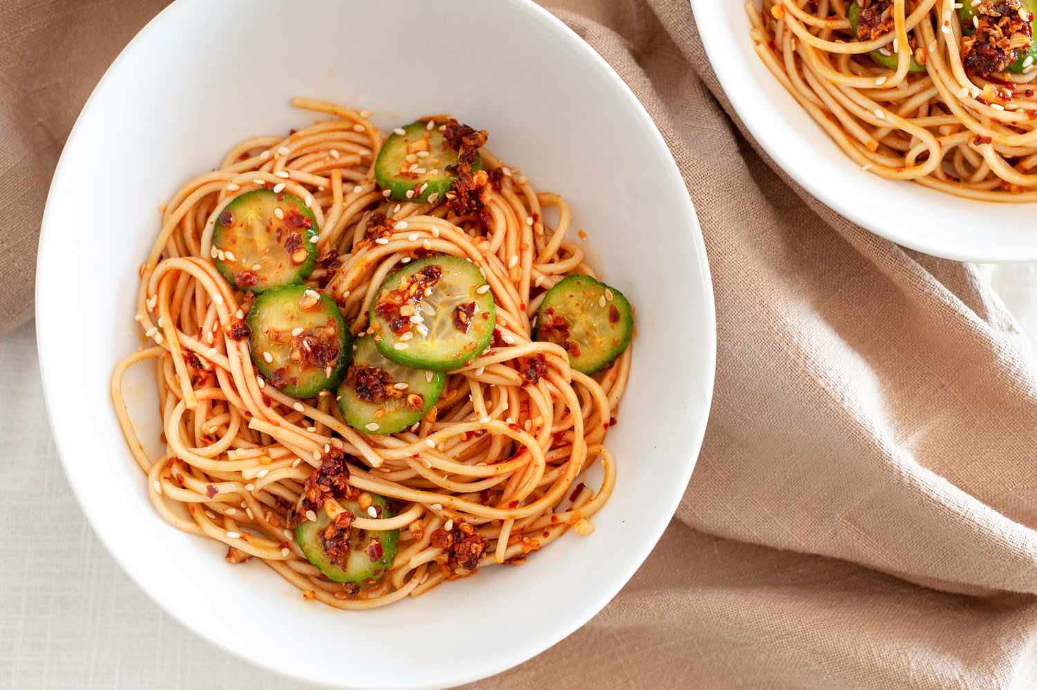 Two bowls of spicy noodles with cucumbers and chili crisp.
